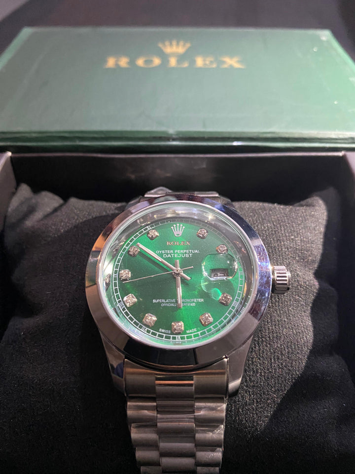 Rolex watch with green dial and silver case on a black cushion, with a green Rolex box in the background.